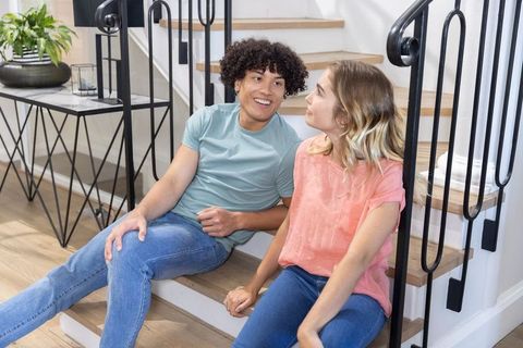 Young couple sitting on staircase smiling and talking inside modern home