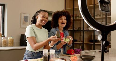 Diverse friends filming healthy cooking tutorial with avocado and cucumber