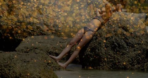 Child relaxing on rocky shore in striped swimsuit with golden bokeh
