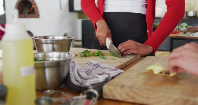 This captures a woman chopping vegetables on a wooden cutting board in a modern and bright kitchen. Ideal for use in articles, blogs, and advertisements related to cooking, healthy eating, culinary tutorials, lifestyle blogs, recipe books, and kitchenware promotions.