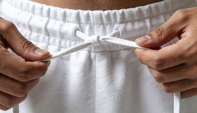 Tying drawstring on white sweatpants closeup showing waistband hands and cotton texture