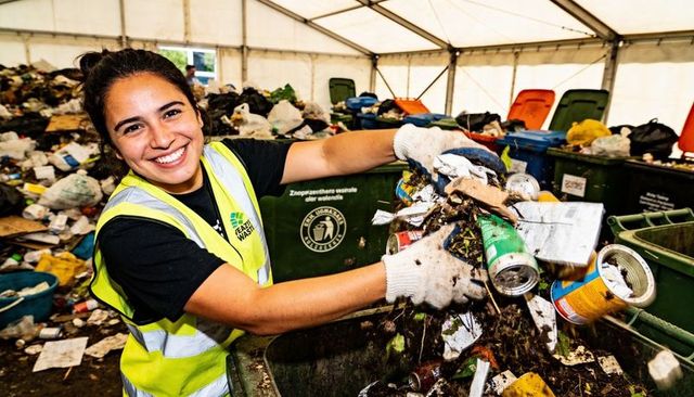Smiling female waste worker sorting cans for recycling in tent wearing hi-vis safety vest