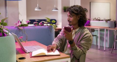 African american man working remotely in pastel coworking space with laptop and phone