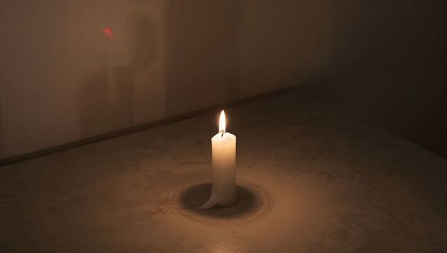 Burning white pillar candle casting warm glow and forming wax ring on patterned table