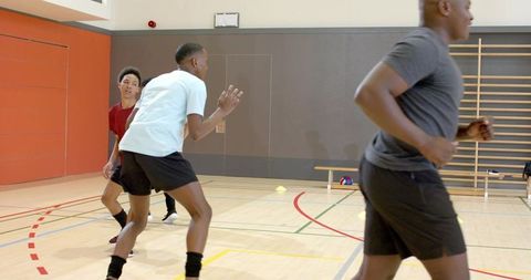 Diverse male students running basketball drills on indoor school gym court