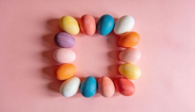 Forming square wreath of colorful dyed easter eggs on pastel pink tabletop, empty center