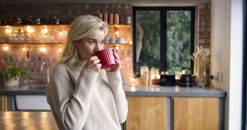 Woman sipping coffee from red mug in cozy modern rustic kitchen, morning light