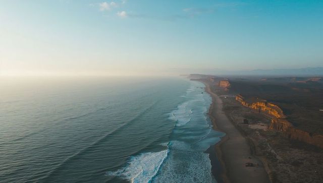 Drone aerial coastline at golden light tracing curving surf lines along sandy beach cliffs