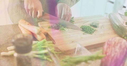 Home cook chopping fresh chives on wooden cutting board with chef knife during meal prep
