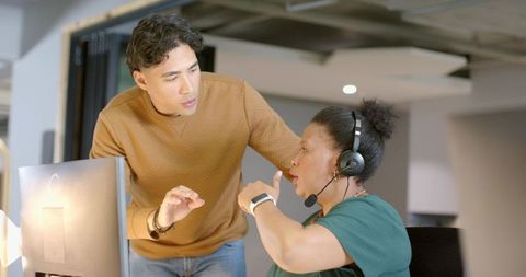 Diverse coworkers collaborating at workstation with headset and monitor in modern office