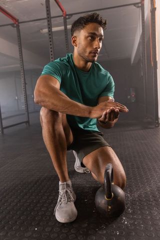 Kneeling athlete rubbing chalk hands beside kettlebell under squat rack