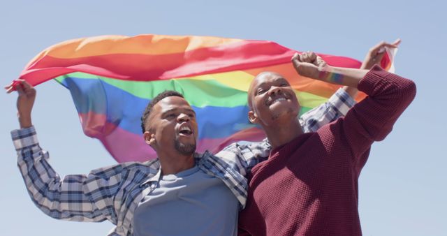 Joyful African American LGBTQ couple seen celebrating outdoors while holding a vibrant pride flag. This imagery captures themes of love, unity, and freedom, perfect for promoting equality, diversity, and pride events. Ideal for use in social media campaigns, awareness posters, or inclusive community initiatives.
