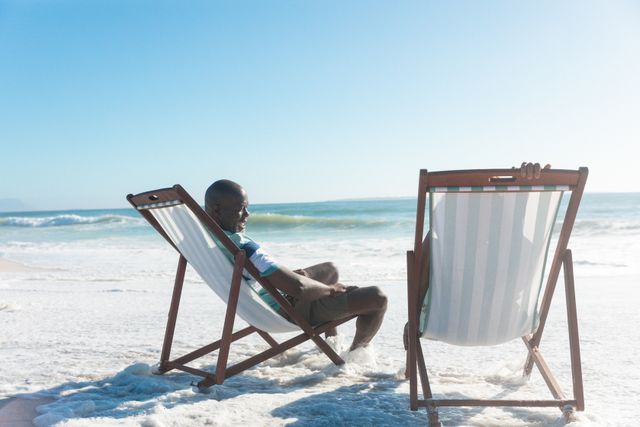 Senior couple enjoying a sunny day at the beach, sitting on folding chairs by the ocean. Ideal for themes related to retirement, leisure, vacations, and outdoor relaxation. Perfect for promoting travel destinations, lifestyle blogs, and senior living.