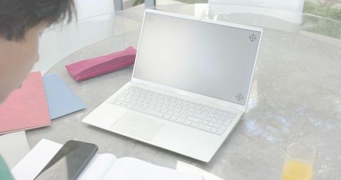 Open white laptop showing blank screen on sunlit round glass table with phone notebooks