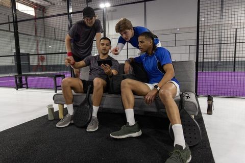 Padel teammates reviewing match strategy on tablet during break at indoor paddle court