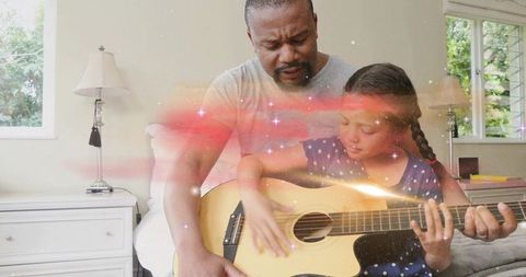 Father teaching daughter guitar in cozy bedroom with warm daylight and dreamy sparkles