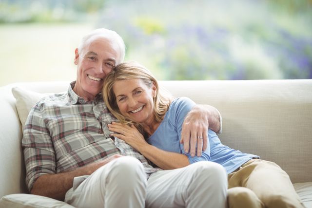 Senior couple sitting together on a sofa, smiling and enjoying each other's company. Ideal for use in advertisements, articles, or brochures related to senior living, retirement, family life, and home comfort. Perfect for promoting products or services aimed at elderly people, such as healthcare, home care, or lifestyle products.