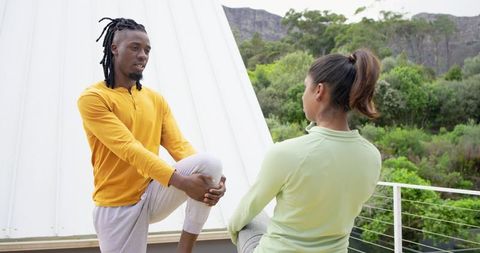 Couple stretching on balcony performing knee-hug stretch for outdoor fitness and wellness