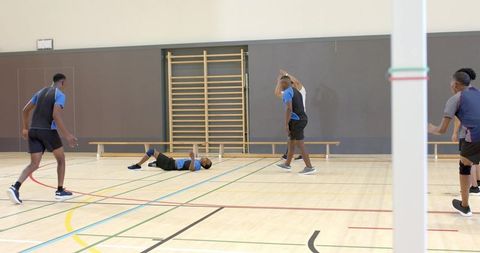 Diverse male sports team supporting fallen teammate on indoor court during training