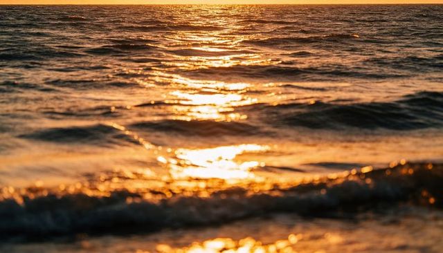 Shimmering golden ocean reflecting sunset light on gentle waves and wet sandy shoreline