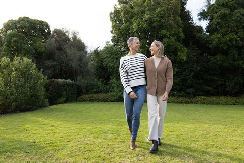Middle-aged women walking arm-in-arm across green park lawn, smiling and chatting
