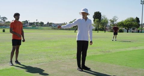 Umpire signaling wide while bowler protesting mid-stride on sunlit cricket field