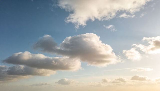 Sunlit cumulus clouds drifting across serene blue sky with golden glow and wispy cirrus