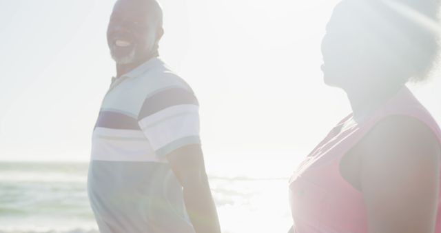 Happy senior african american couple holding hands on sunny beach at sunset, copy space. Retirement, summer, vacations, togetherness and senior lifestyle, unaltered.