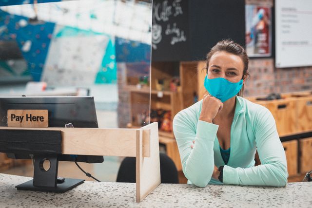 Caucasian woman wearing face mask leaning on counter at reception of indoor climbing gym. fitness and leisure during coronavirus covid 19 pandemic.