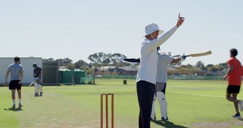Cricket umpire signaling out raising finger wearing wide hat and whites on sunny outfield