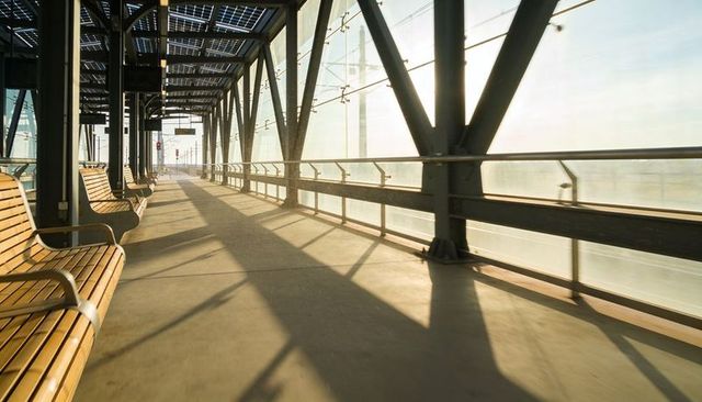 Empty Sunlit Elevated Train Platform Basking in Morning Light with Wooden Benches and Solar Panels