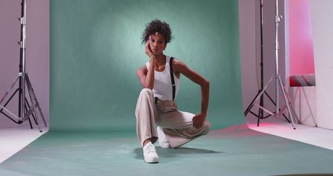 Curly haired african american model kneeling on mint backdrop with sneakers and suspenders