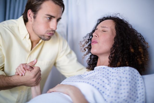 Man holding pregnant woman's hand while she is in labor in hospital. Useful for topics related to childbirth, maternity care, family support during labor, and healthcare services. Ideal for articles, blogs, and educational materials on pregnancy and childbirth.