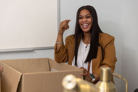African american businesswoman laughing and packing office box, relocating and organizing