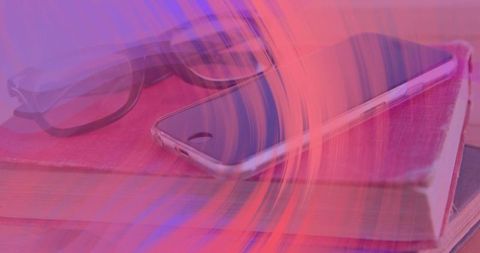 Magenta light swirl washing over smartphone and notebook with glasses on wooden desk