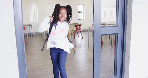 Youthful student entering classroom with backpack and polka dot sweater