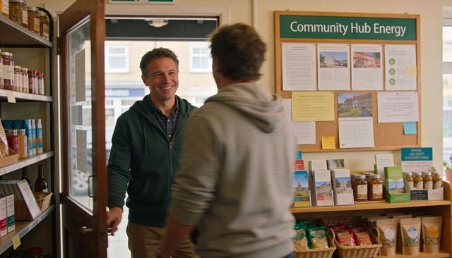 Smiling volunteer welcoming visitor in community hub doorway, cozy local shop interior