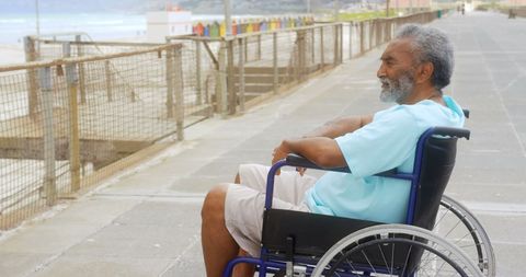 Senior Man in Wheelchair Reflecting by Seaside Promenade