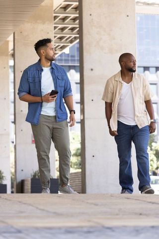 Two men of african descent walking under concrete overhang at office plaza with smartphone