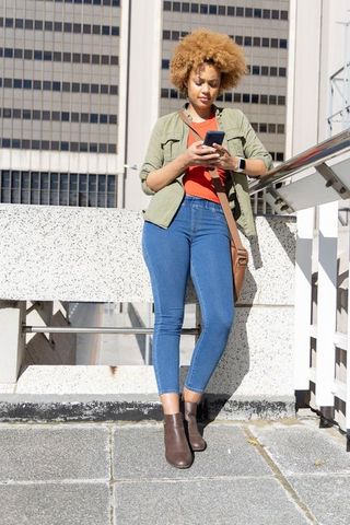 African american woman leaning on rooftop railing checking smartphone during urban commute