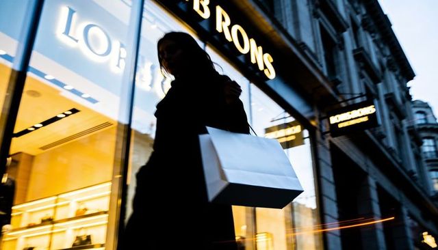 Silhouetted shopper walking past luxury storefront at dusk carrying white shopping bag