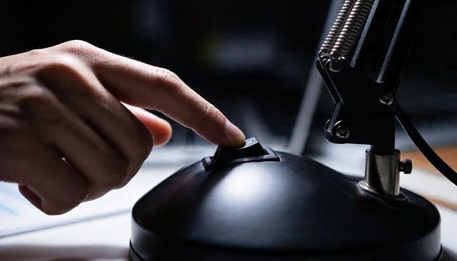 Pressing finger on desk lamp switch on glossy black base closeup with metal arm
