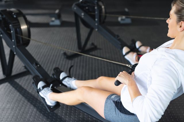 Caucasian woman using a rowing machine in a gym, focusing on fitness and health. Ideal for promoting active lifestyles, gym memberships, fitness equipment, and workout routines.