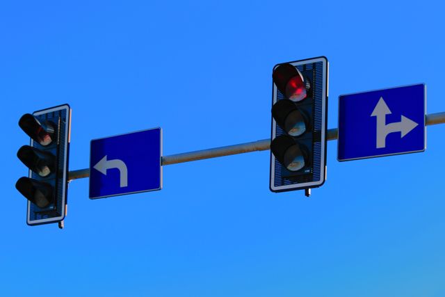 Traffic lights and directional road signs are hanging beneath a clear blue sky. Image highlights traffic control systems, urban planning, and road safety. Suitable for use in transportation articles, urban planning presentations, or educational materials on road safety.