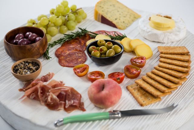 Variety of cheese with grapes, olives, salami, crackers and knife on wooden board