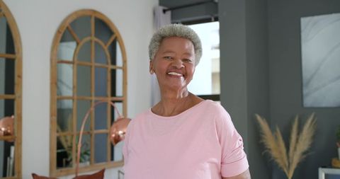 Smiling senior black woman standing in modern cozy living room with arched mirrors