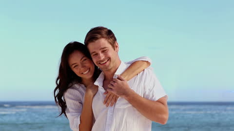Smiling Couple Embracing On Beach Against Blue Sky