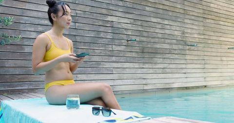 Woman Relaxing by the Poolside with Smartphone in Yellow Swimsuit