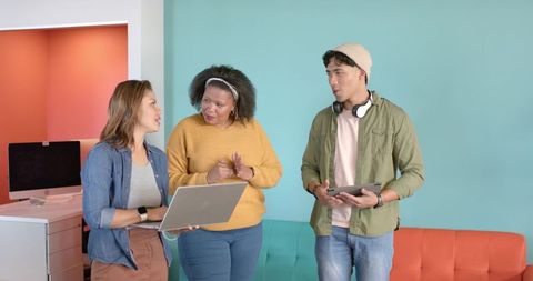 Diverse team discussing project using laptop and tablet in bright modern coworking space