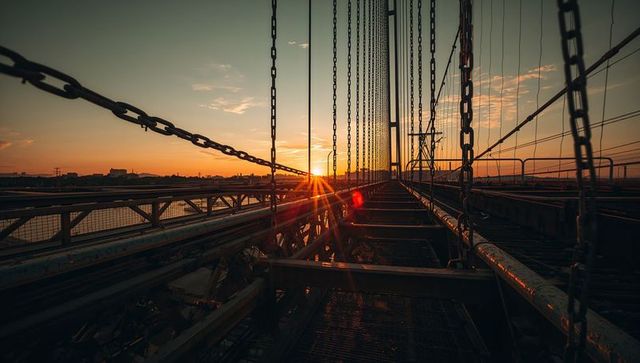 Sunset aligning with suspension bridge walkway guiding view toward support tower